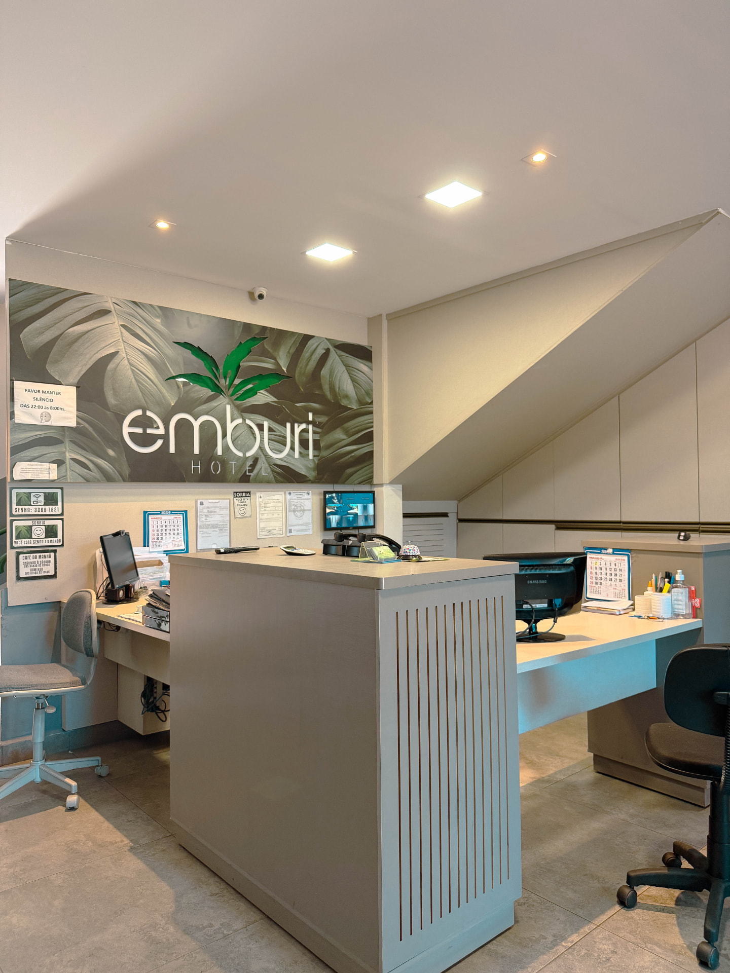 Recepção do Emburi Hotel com painel de folhagens e logotipo